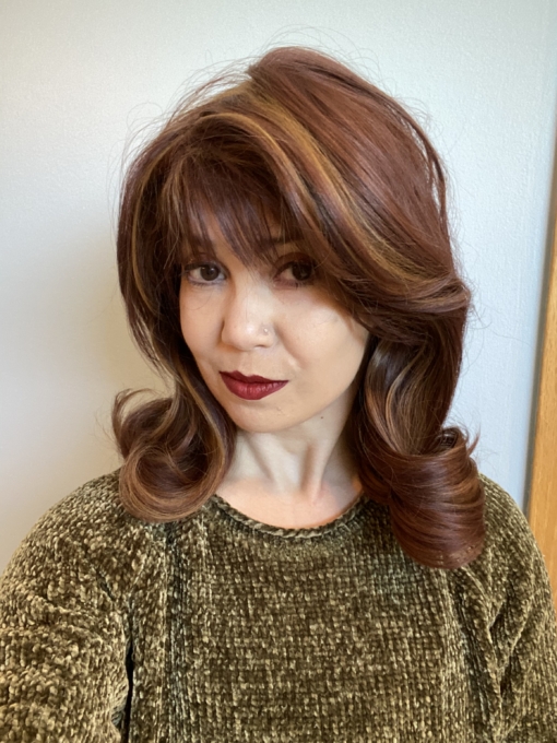 Film Star is a warm chestnut brown with golden highlights throughout. The style is sleek from the roots, ending in large curls. The bangs are  blunt and sleek.