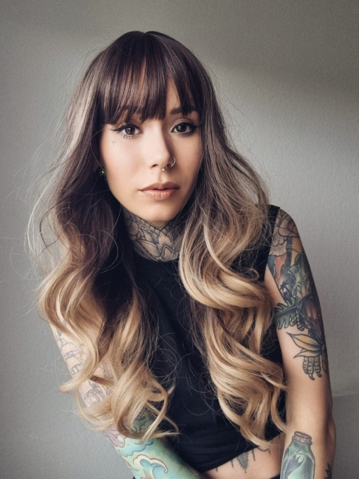 A long and sleek wig with natural dark brown shadowed roots. They blend into a sandy blonde with highlights of platinum blonde that mix beautifully to create this colour. Cut with long layers and a long fringe that can swept to the side or parted into curtain bangs.