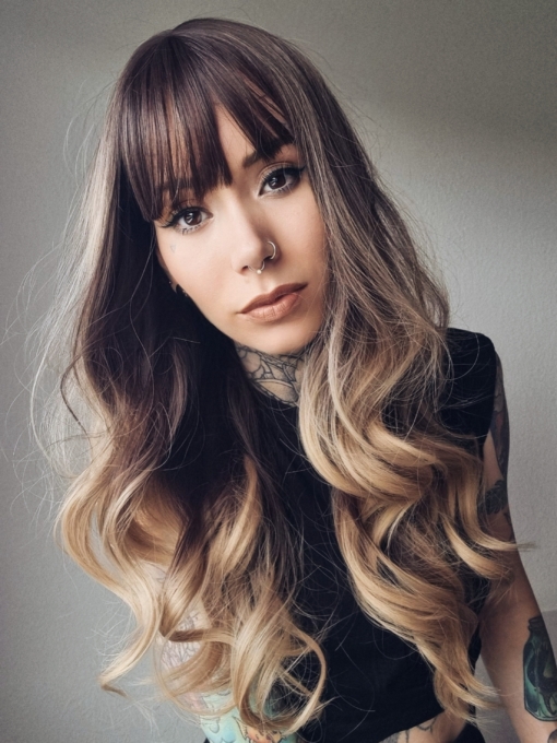 A long and sleek wig with natural dark brown shadowed roots. They blend into a sandy blonde with highlights of platinum blonde that mix beautifully to create this colour. Cut with long layers and a long fringe that can swept to the side or parted into curtain bangs.